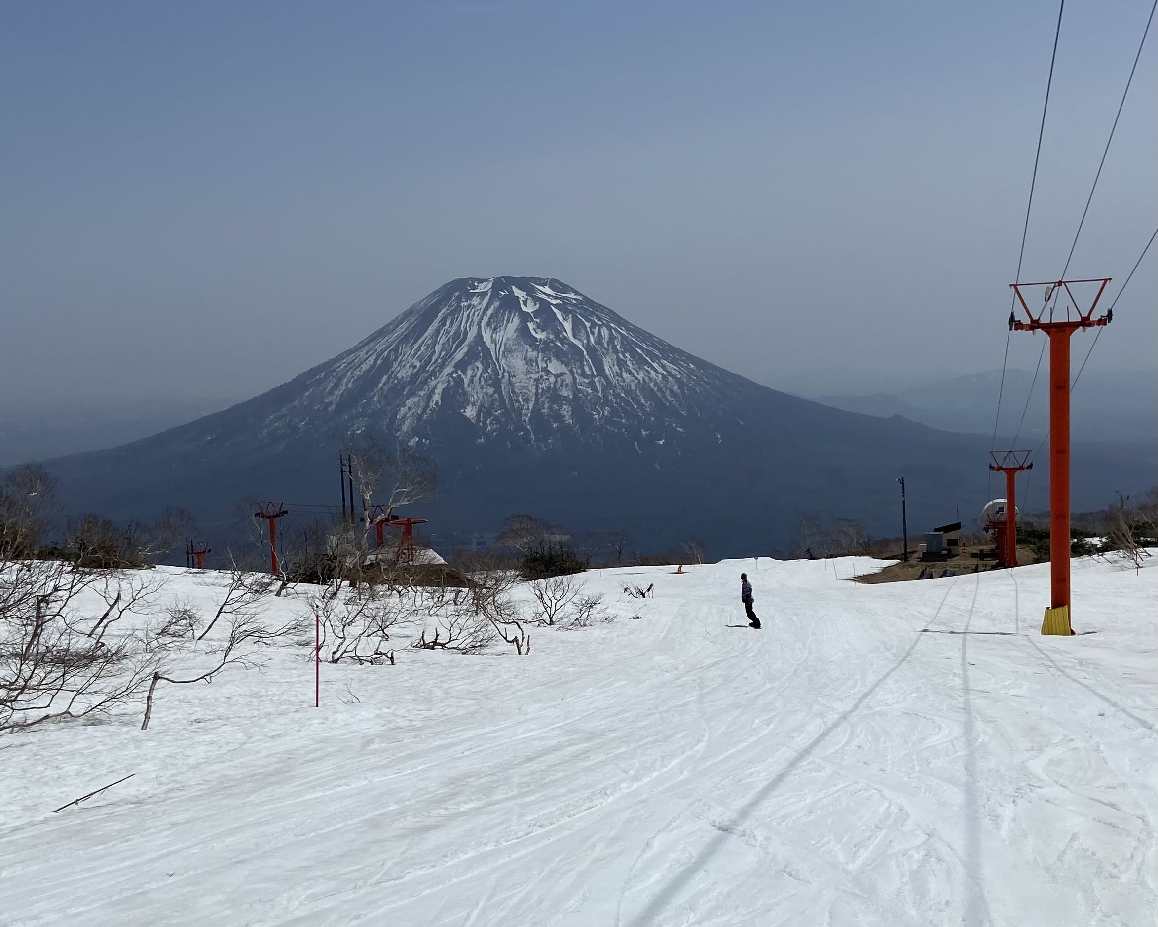 A snowboarder rides a strip of snow toward Mount Yotei