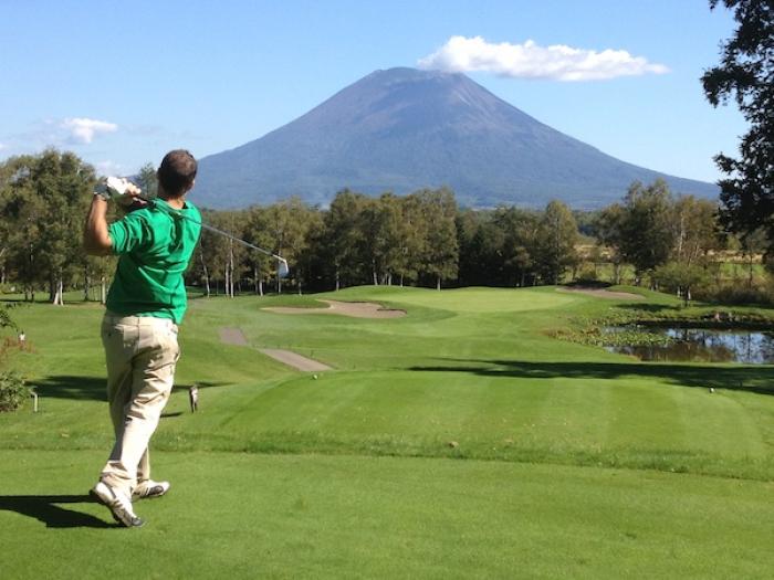 A golfer drives down a fairway with Mount Yotei in the back ground
