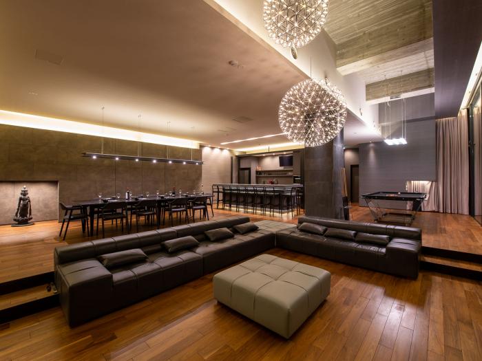 A black sofa with dining table behind and round chandelier above