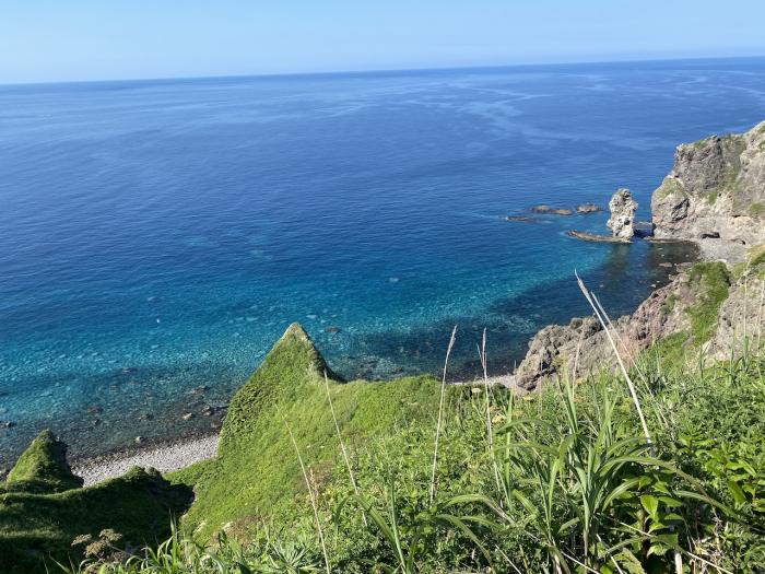 Steep vegetation covered cliffs over a blue sea
