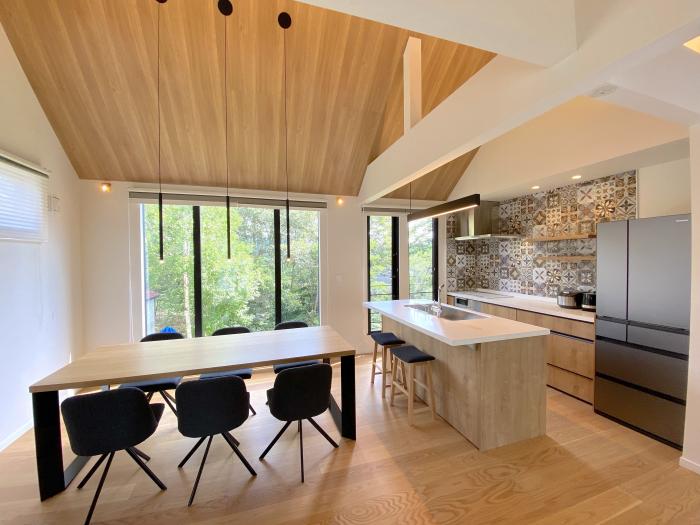 A kitchen area with dining table and seating for six, kitchen island and patterned splash back.
