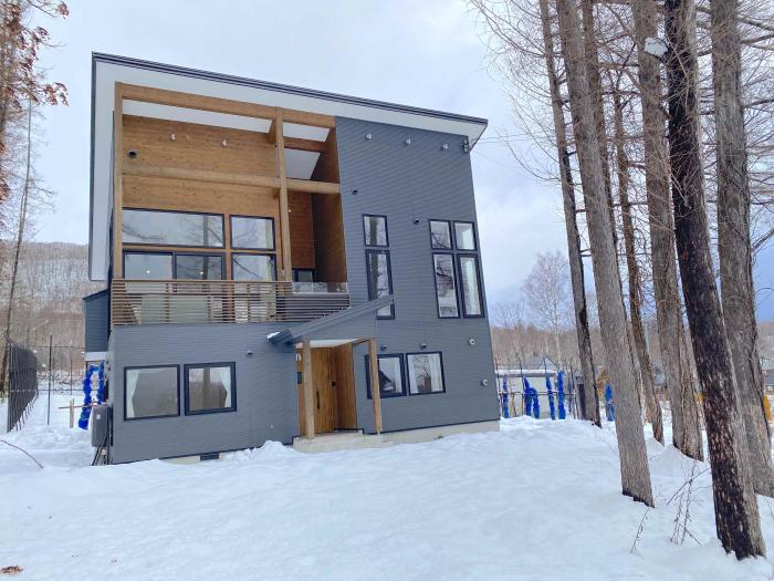 A two story home with trees to the right and snow in the foreground