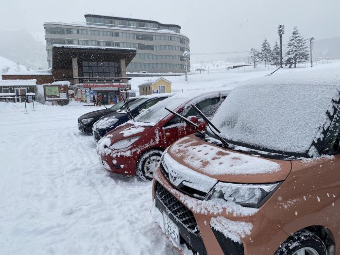 A row of cars with their wipers up and the Hirafu Welcome Center in the back ground