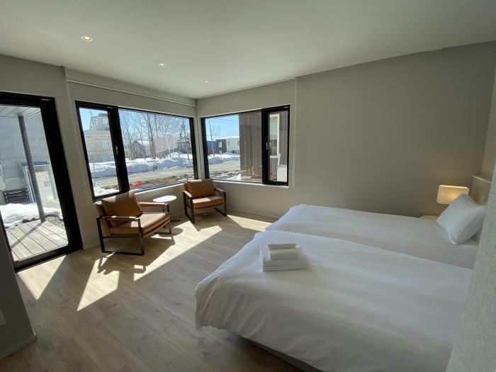 A bedroom with white beds and chairs in a sunny corner