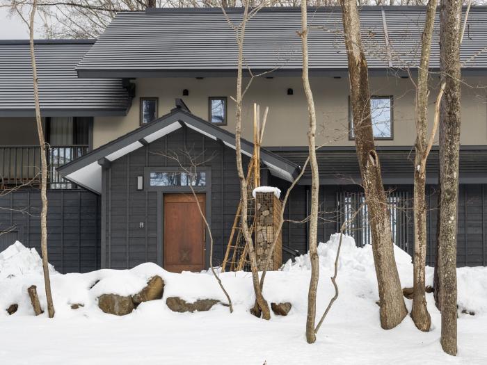 Nagare House in Niseko, Japan: A contemporary mountain chalet with dark wood exterior and natural stone entrance, surrounded by birch trees and deep snow, perfect for luxury ski holidays