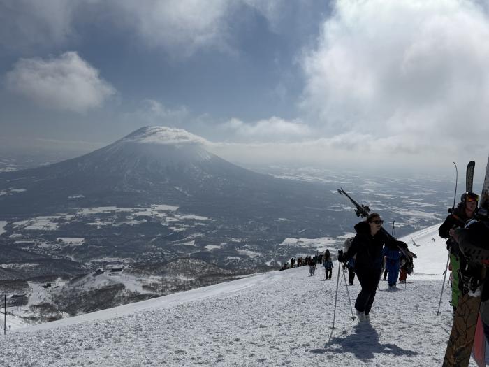 Skiers hike up a slope with Mount Yotei in the background