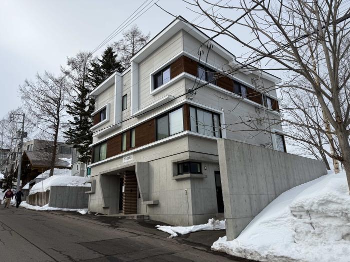 Exterior view of modern Yutaka Townhouses in Niseko, featuring contemporary architecture with wooden accents, surrounded by snow-covered landscape, within walking distance to Hirafu ski lifts.