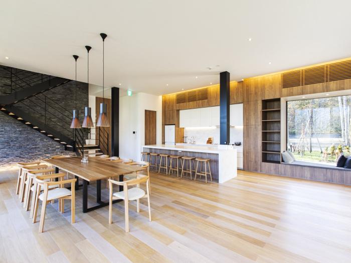 Modern open-concept luxury chalet interior in Niseko with natural wood floors, designer kitchen, and expansive dining area surrounded by forest views - perfect for premium ski holidays in Japan.