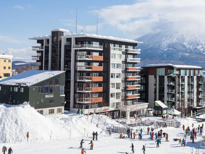 Alpen Ridge luxury ski-in ski-out accommodation at Niseko ski resort with modern apartment buildings adjacent to snow-covered slopes and skiers enjoying powder snow conditions with mountain views