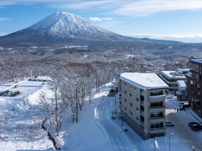 A snow covered landscape with Mount Yotei behind and hotel building to the right