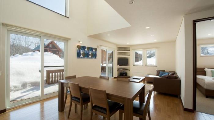 wooden dining table with large windows and living space in background