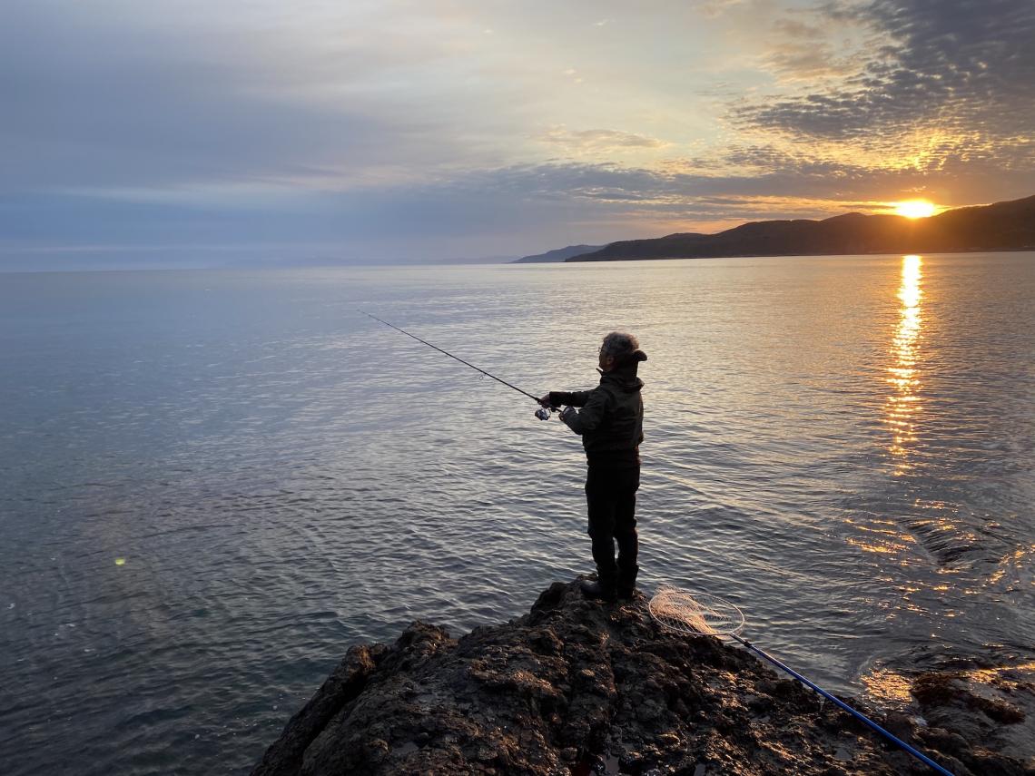 The silhouette of a man fishing in the ocean at sunrise