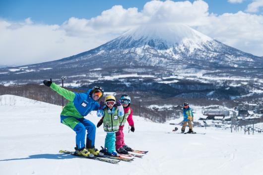 A ski instructor and two children pose on a ski slope with Mount Yotei in the back ground