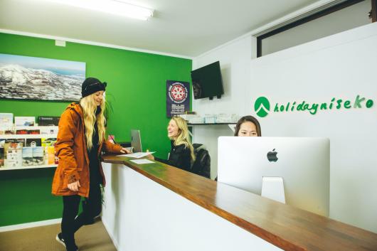 A blonde woman customer stands at the holiday Niseko front desk staffed by 2 people.