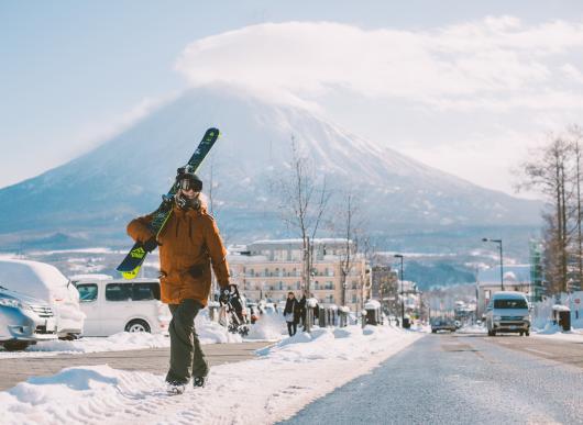 walking up main street of Hirafu carrying skis