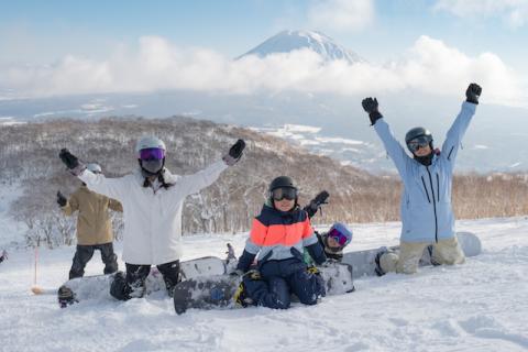 Four kneeling snowboarder raise their arms for the camers