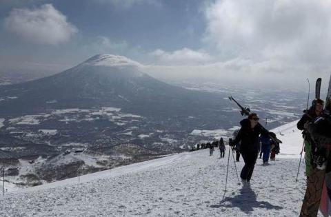 A line of skiers and snowboarders hike up a slope