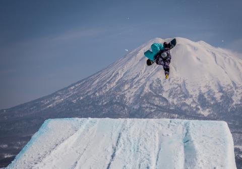 A snowboard does a jump with Mount Yotei in the background