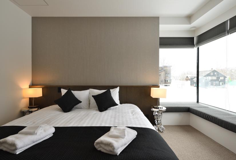 large bed with black pillows, lamps, and corner window