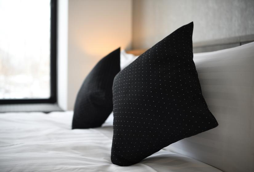 black pillows on white bed with bedside light in background