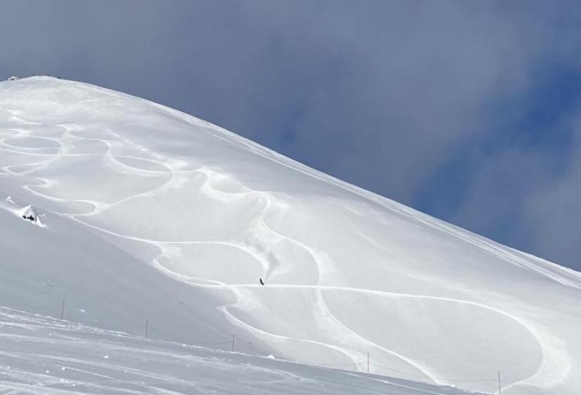 A snowboarder makes a turn with blue skies above