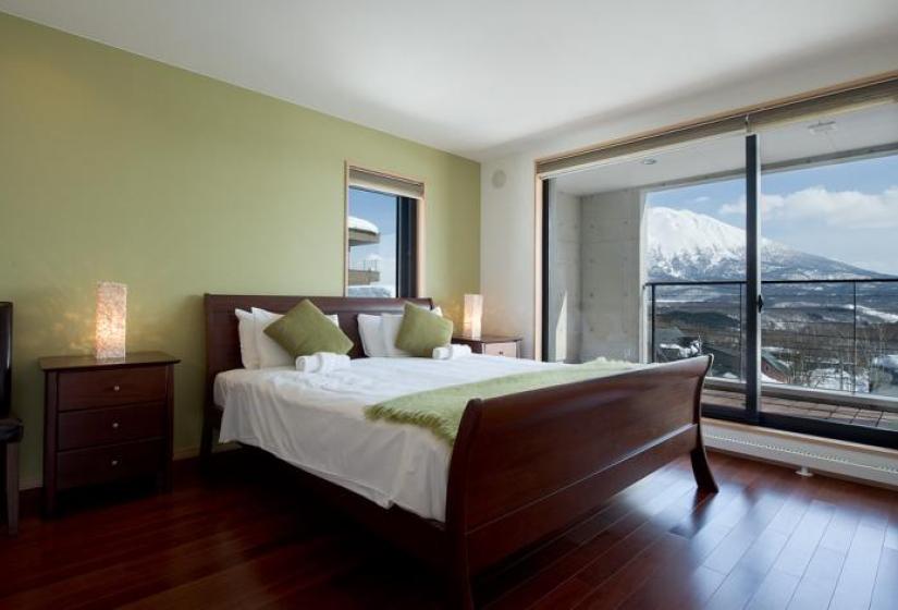 A made up double bed with white towels and tan cushions in a room with a mountain back drop