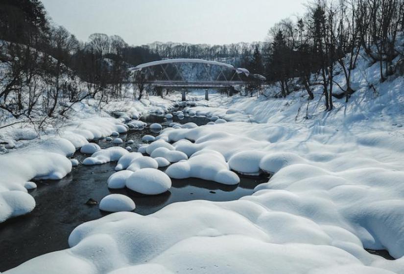 A snowy river scene with a blue bridge in the background.