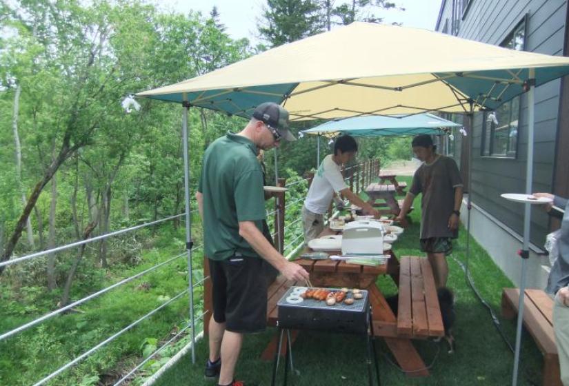 A man tends a bbq with bbq tables and marquee in the back ground