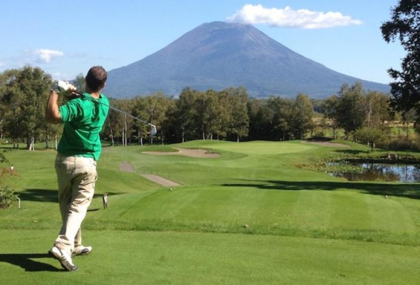 A golfer drives down a fairway with Mount Yotei in the back ground