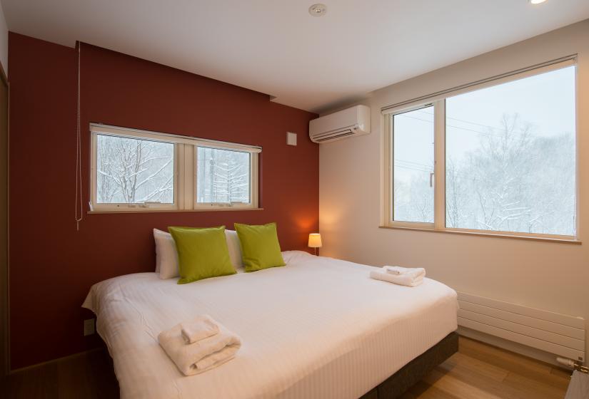 king bed with white sheets and green pillows. two walls with windows