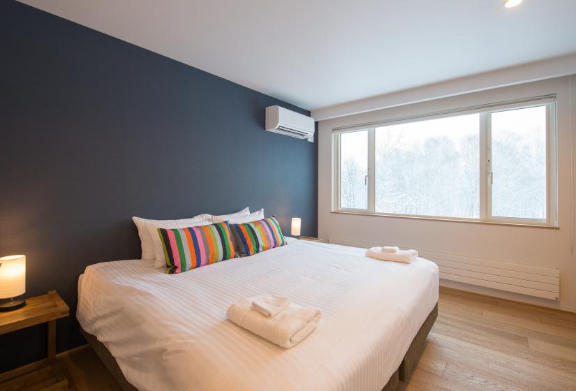 king bed with rainbow pillows, blue wall, and window