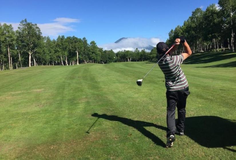 A golfer drives down a fairway at Hanazono with Mount Yotei in the distance