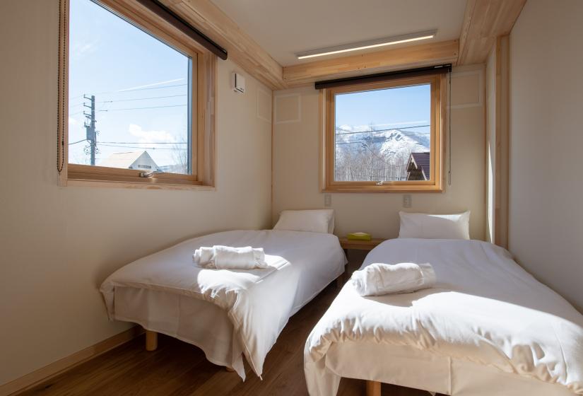 Two single beds with white linen under 2 windows
