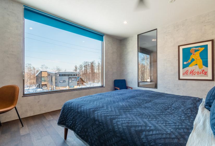Bed with blue bed spread and view of houses in the distance 