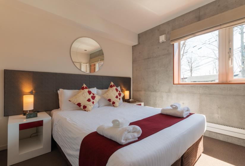 large bed with white sheets, mirror above headboard and window