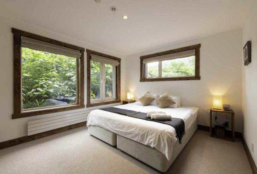 A made up double bed with black throw, rolled towels and brown pillows