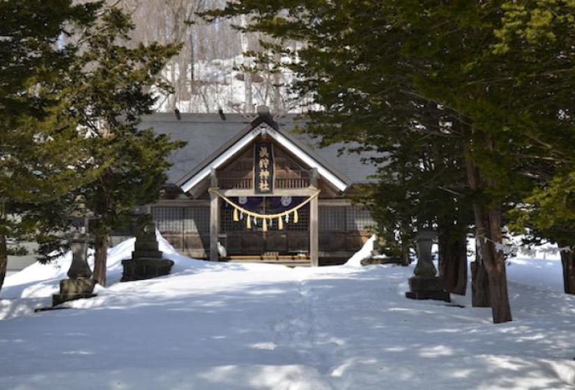 A small wooden shrine surrounded by snow and framed by trees
