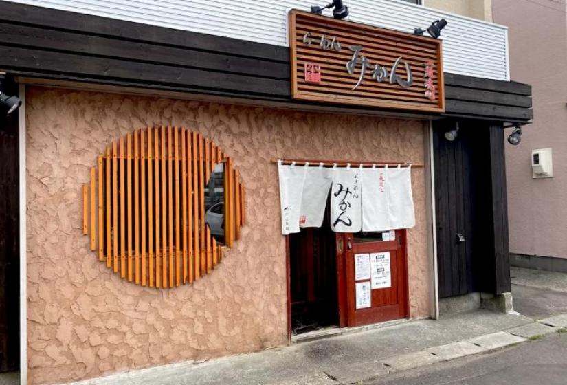 Exterior of a ramen shop with round slatted window and flags above door