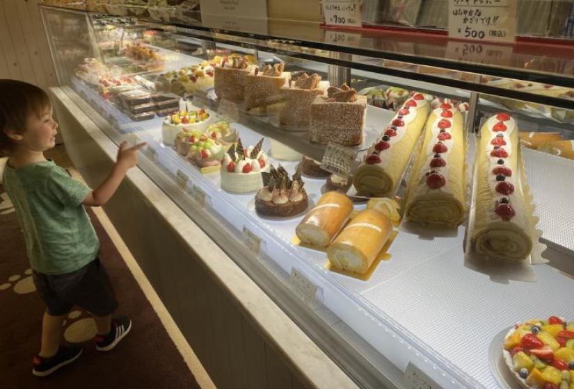 A child points toward a display case of colourful cakes