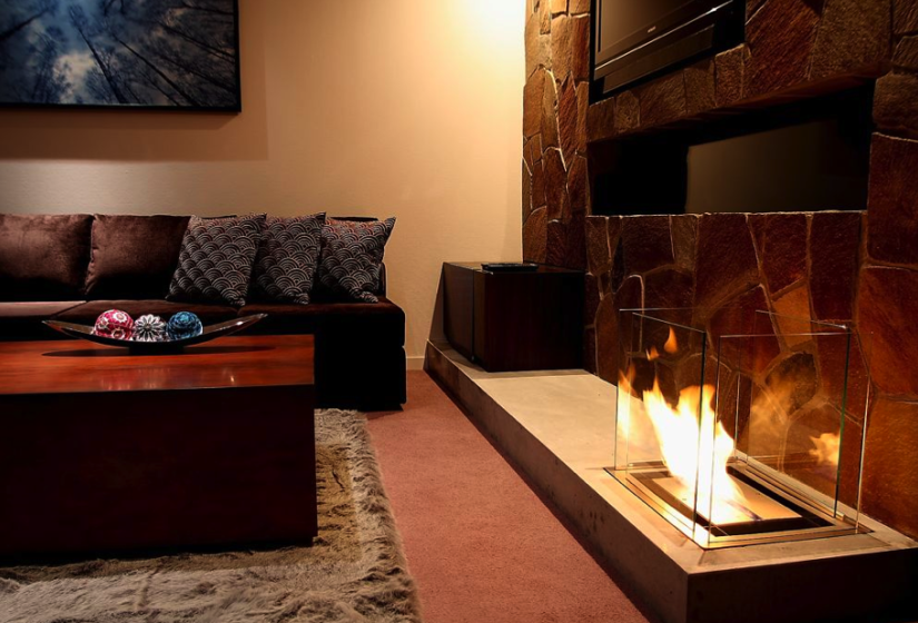 fireplace with black leather couches, stone faced wall, and wooden coffee table