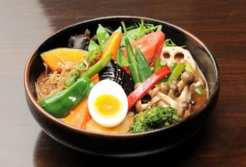 A bowl of curry with egg, egg plant, broccoli and mushrooms.