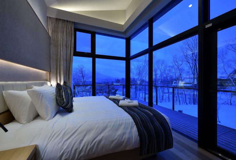 A double bed with white duvet faces a corner window