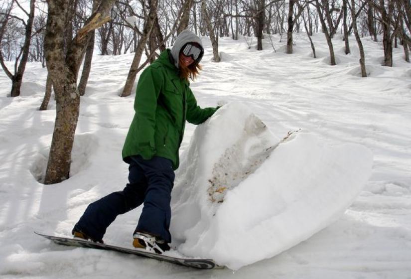 A snowboarder stands beside a large fallen snow block.