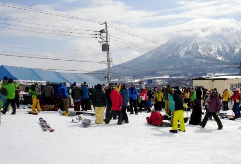 A large group of skiers and snowboarders with Mount Yotei in the back ground