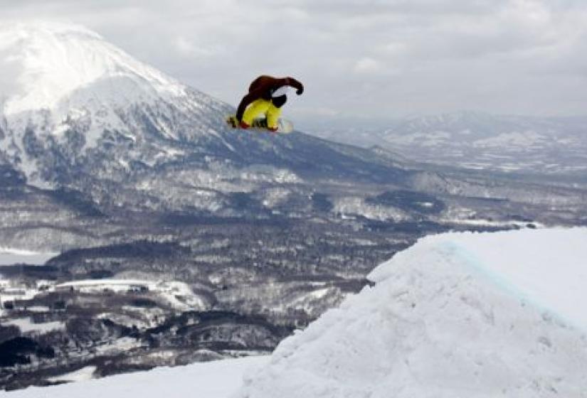 A snowboarder spinning of a large table top jump