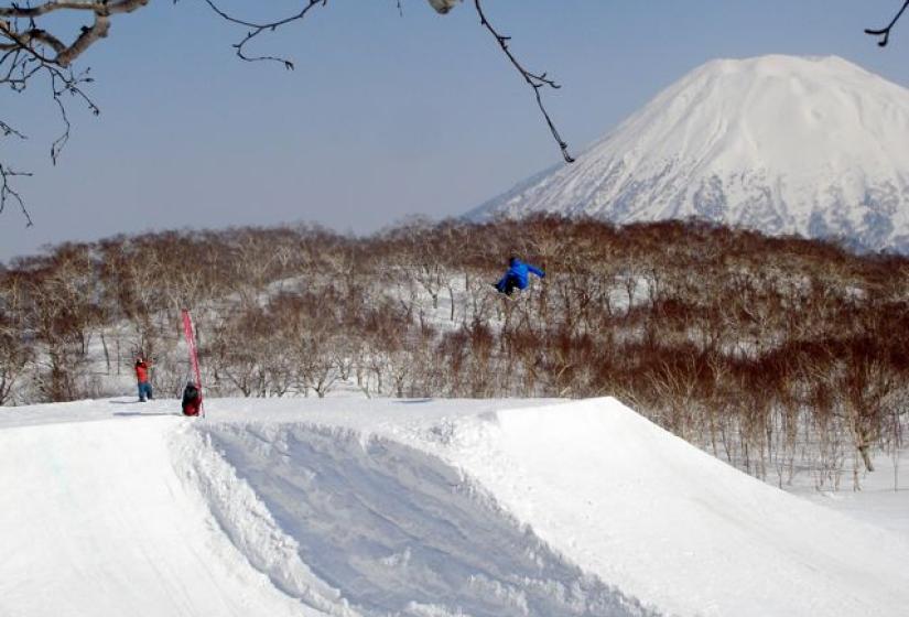 A snowbaorder jumping with Mount Yotei in the background