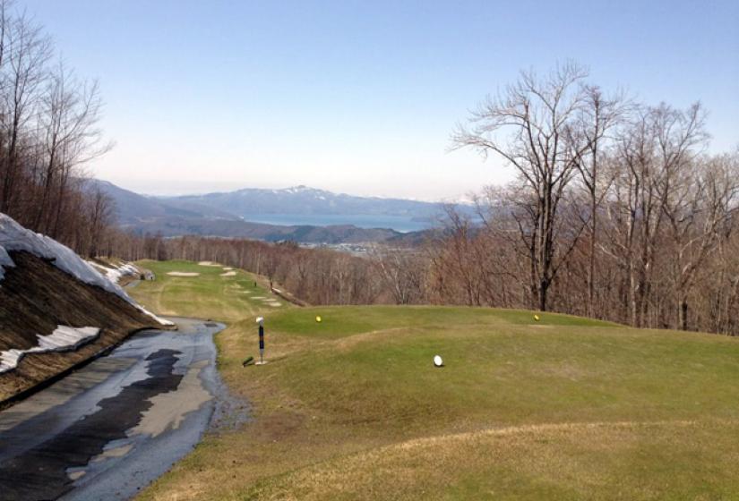 A golf course with sparse trees and blue skies.