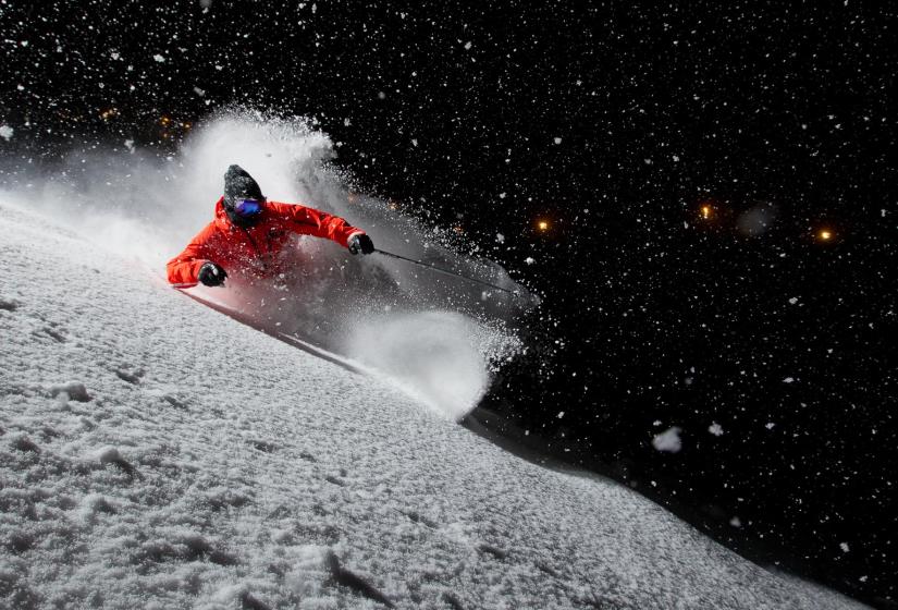 A skier makes a turn with their spray illuminated in the darkness