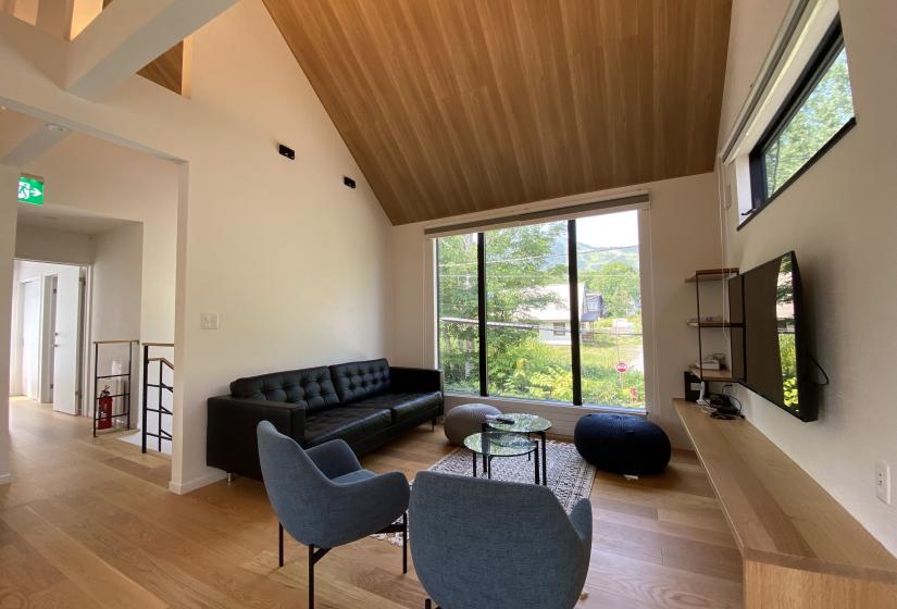 A living room with large windows behind a black lounge suite and 2 arm chairs