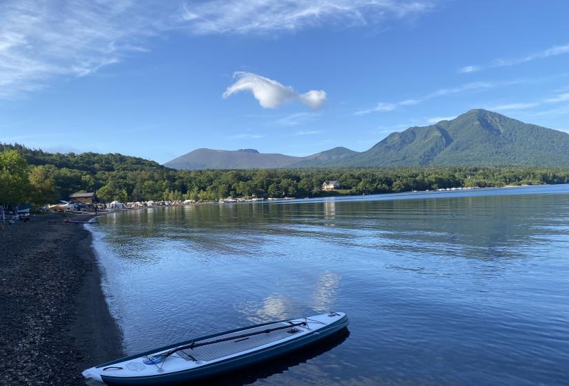 A stnd up paddel board lies at the side of a glassy lake with rolling hill surrounds.